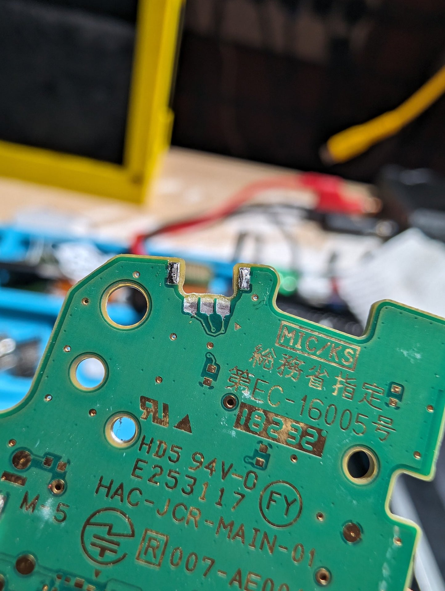 Close-up of a green electronic circuit board with text and symbols. Switch Joy-con with ripped pads for R button